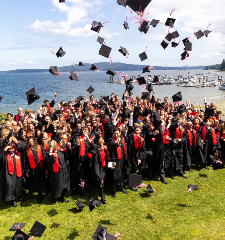Schüler in Talar werfen am Graduation Day ihre Hüte in die Luft und jublen.