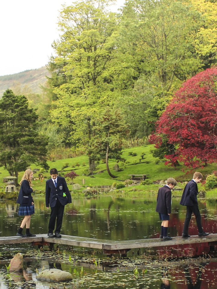SchülerInnen der Dollar Academy wandeln beim Besuch in Cowden Garden auf einem Steg über den Teich.