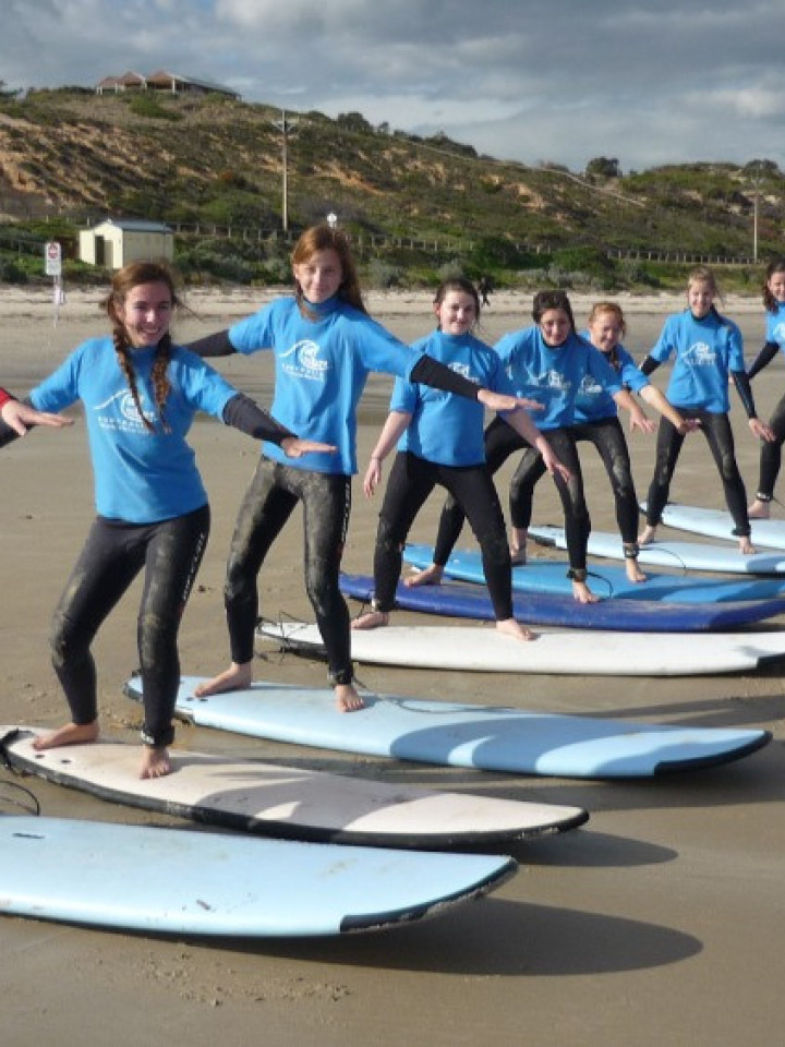 Schülerinnen machen Trockenübungen auf Surfbrettern am Strand.