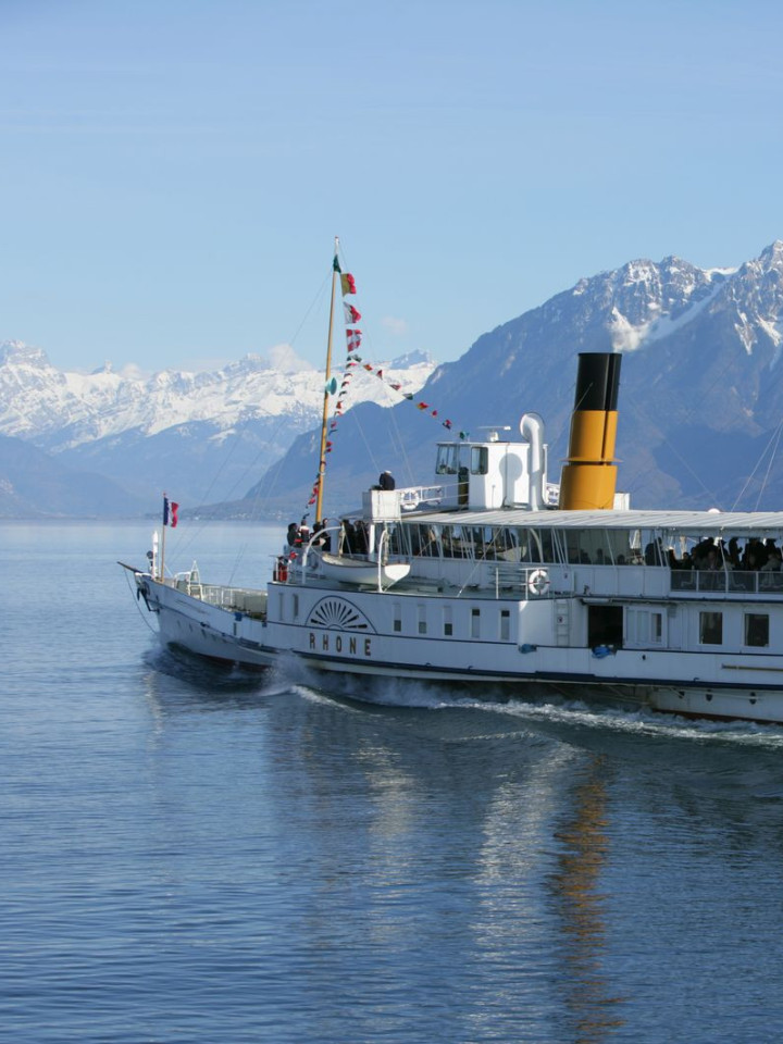 Schiff auf dem Genfer See mit Schweizer Flagge und Bergen im Hintergrund.