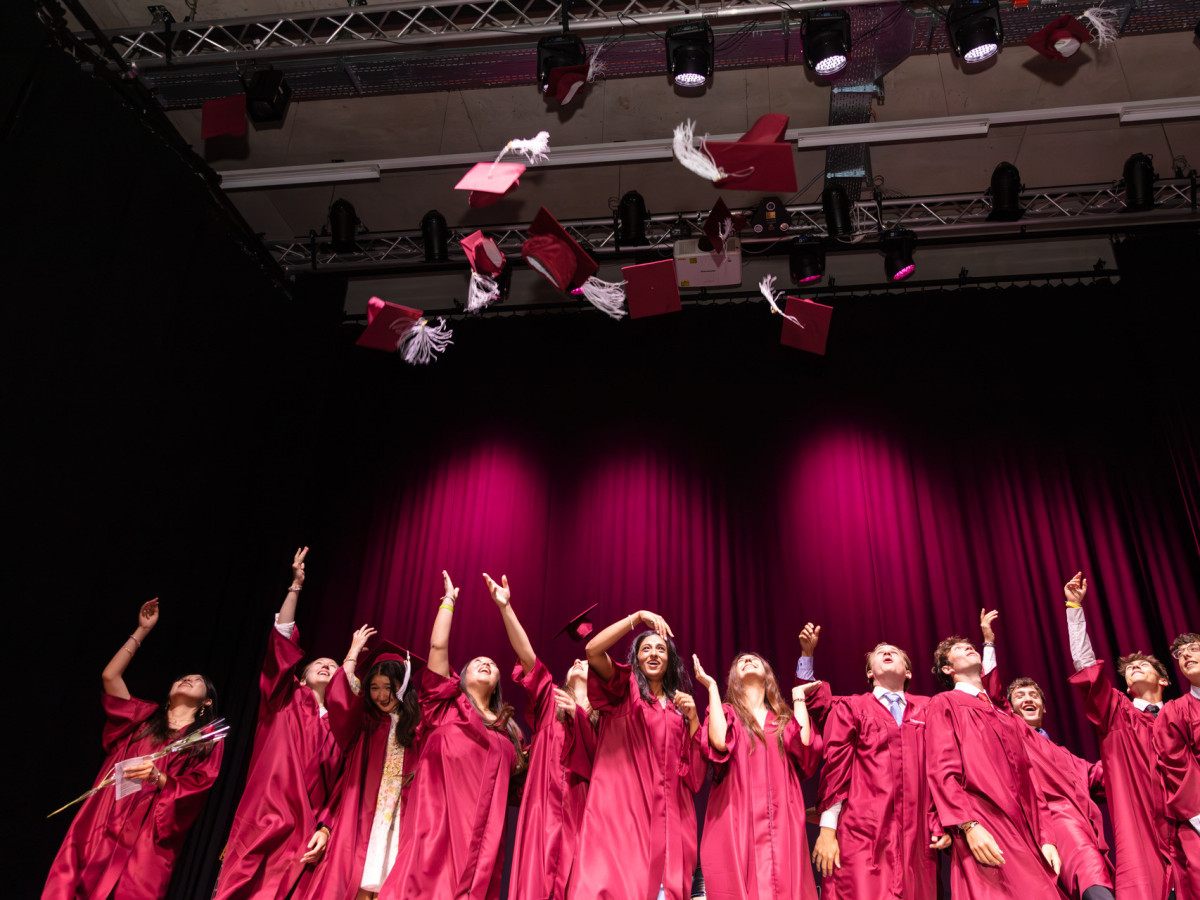 Schülerinnen und Schüler beim Graduation Day in Talar mit fliegenden Hüten
