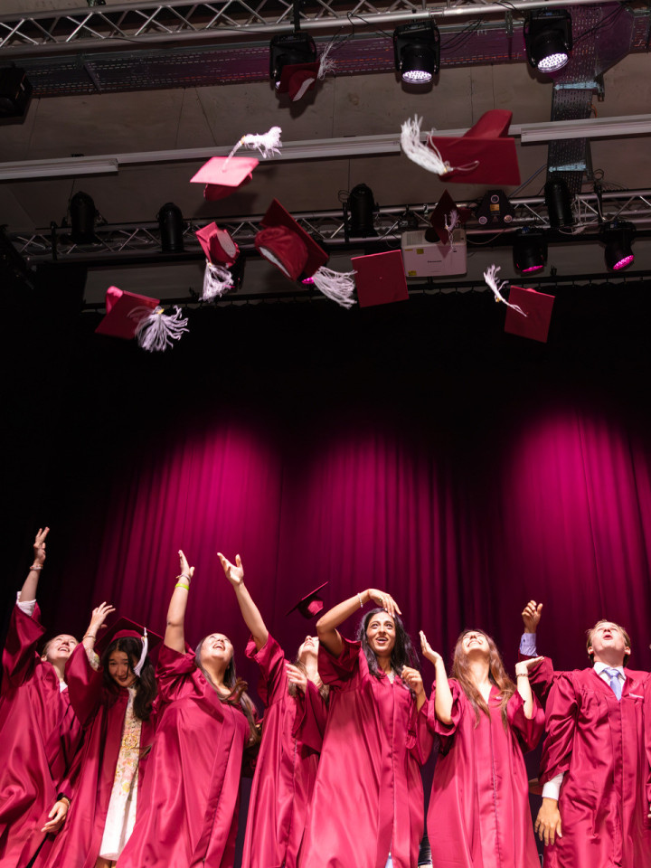 Schülerinnen und Schüler beim Graduation Day in Talar mit fliegenden Hüten