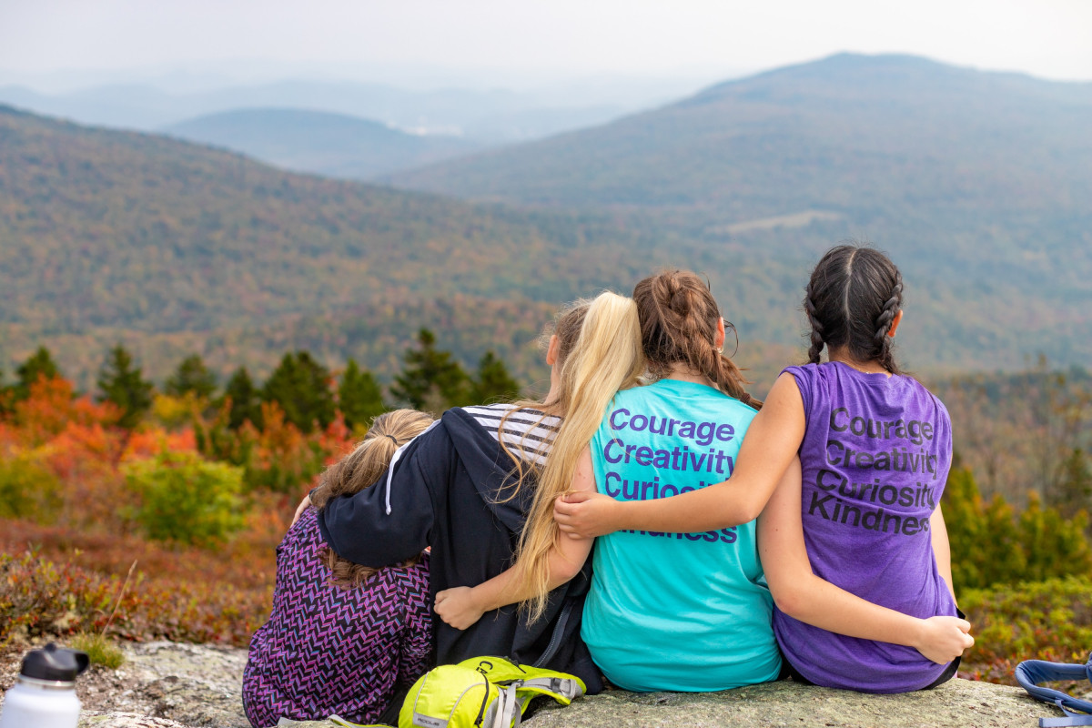 4 Schülerinnen der Gould Academy auf Felsen sitzend mit Blick ins Tal und  Berge.
