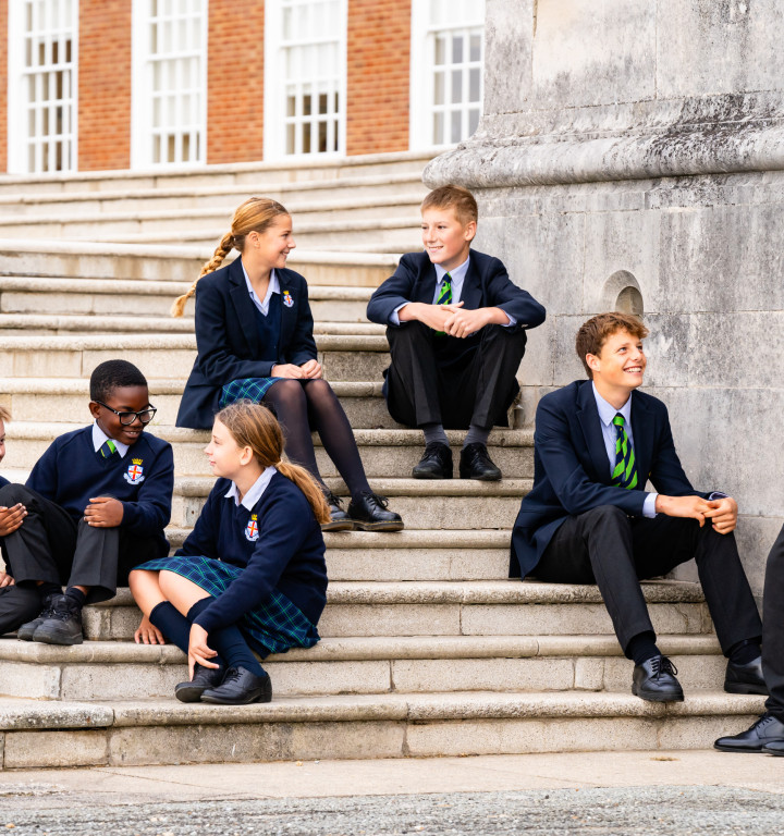 Schülerinnen und Schüler in Unfiform sitzen auf den Stufen des historischen Hauptgebäudes