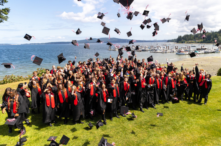 Schüler in Talar werfen am Graduation Day ihre Hüte in die Luft und jublen.